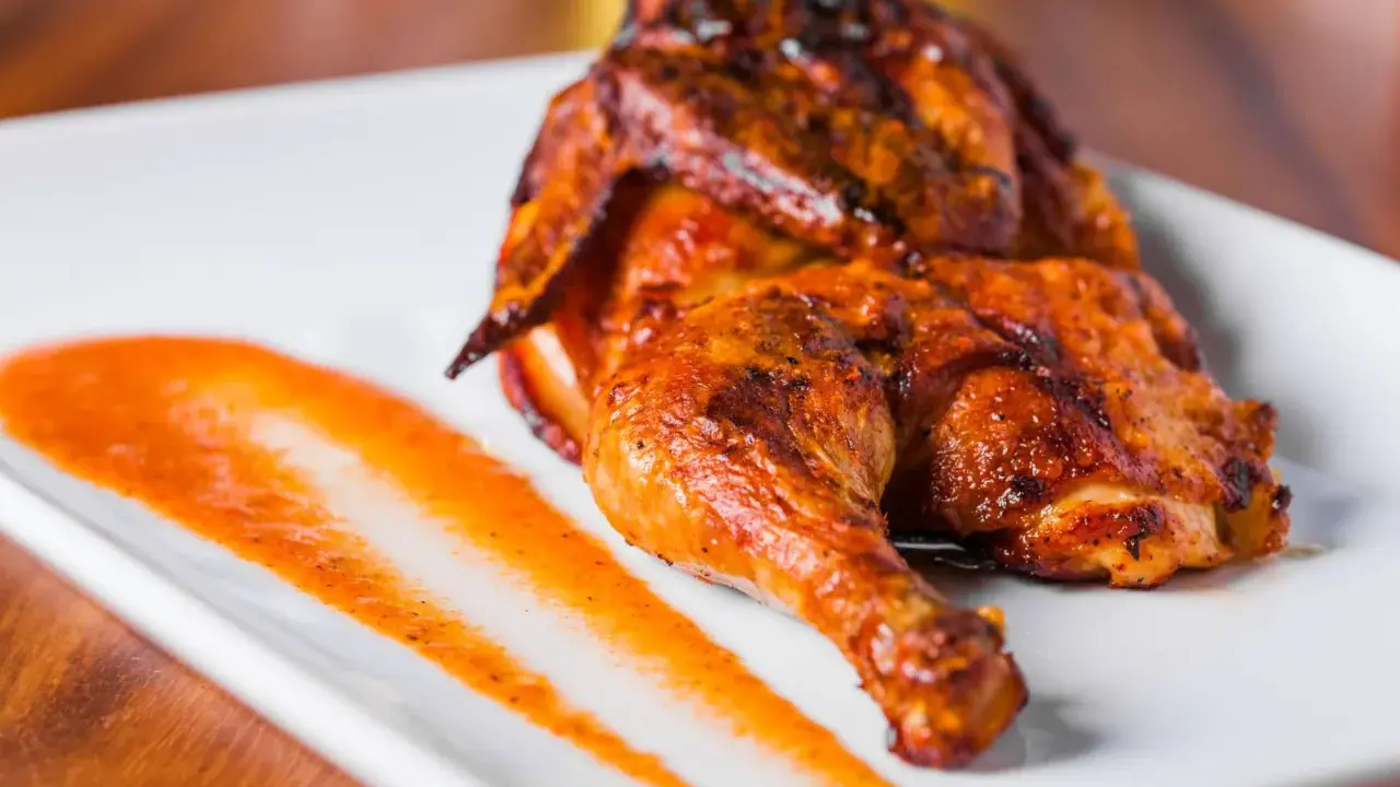 Un délicieux poulet portugais au four, la peau dorée et croustillante, servi avec une sauce épicée sur une assiette blanche.