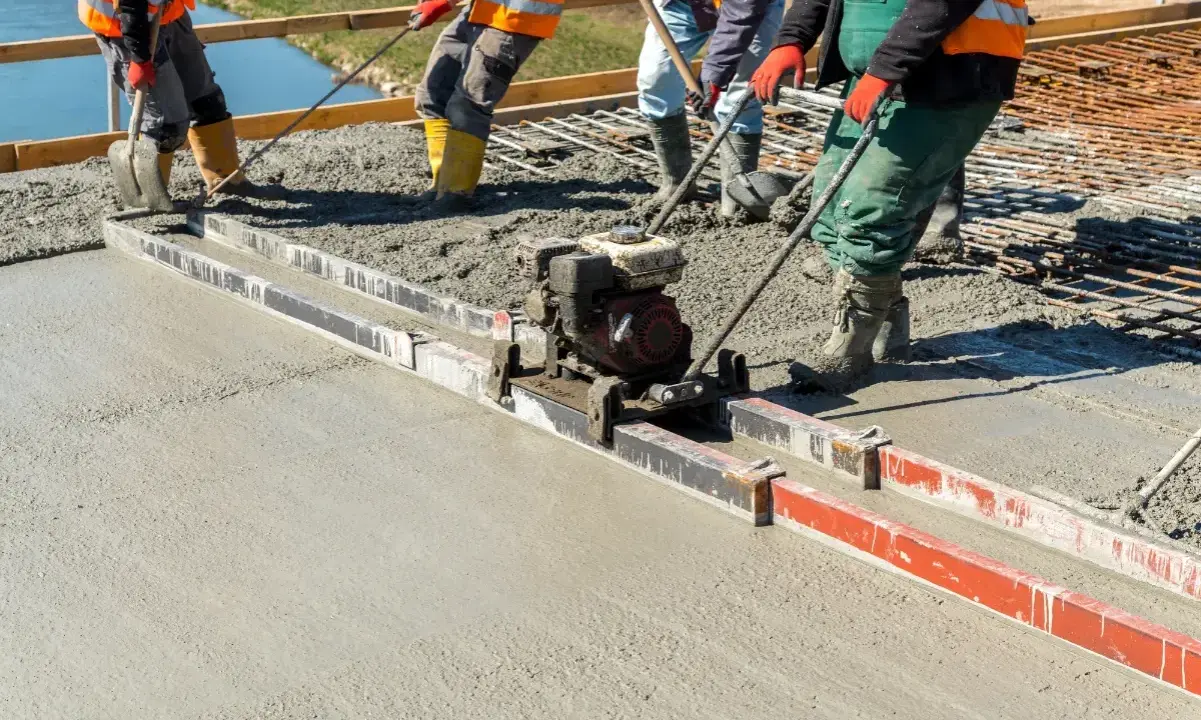 Budowlańcy używają wibrołaty do wyrównania świeżego betonu na budowie.
