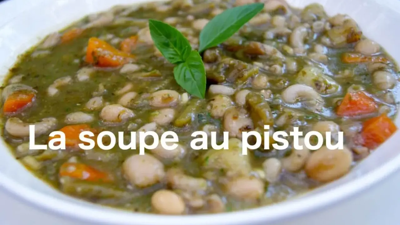 Un bol de soupe au pistou, garni de basilic frais, avec des haricots blancs, des pâtes et des carottes.