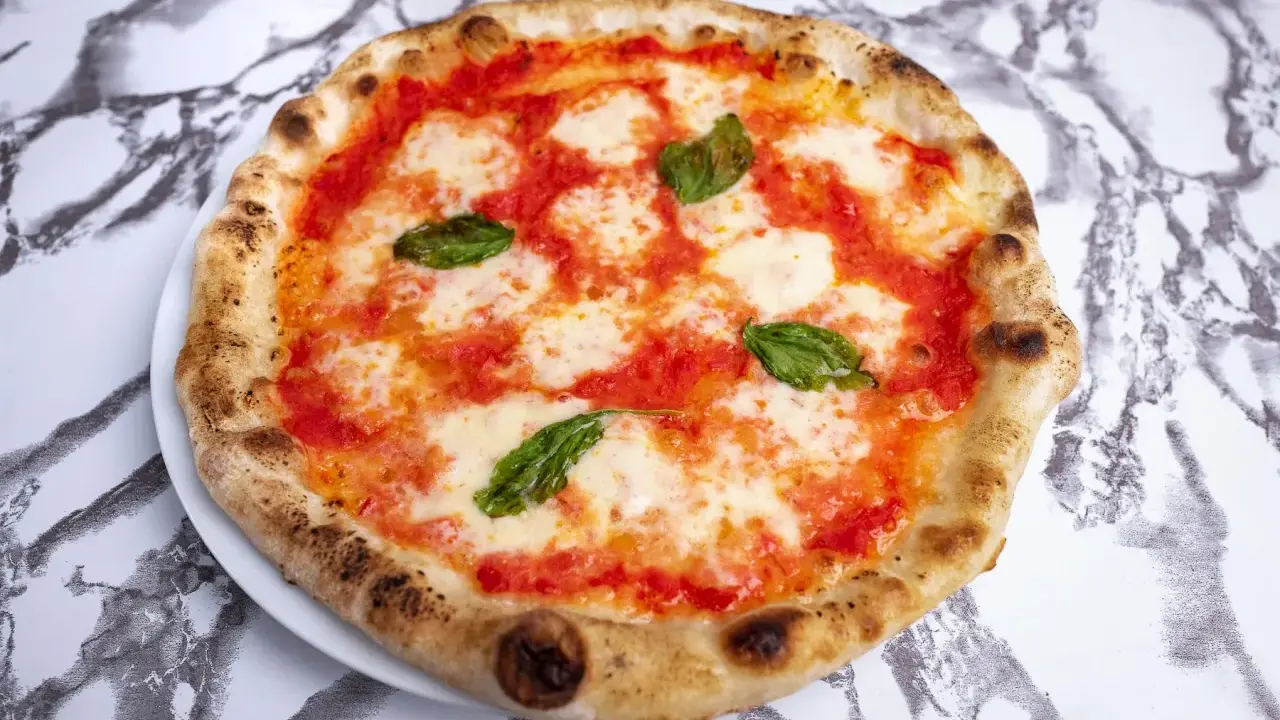Pyszna pizza napoletana z pomidorami, mozzarellą i bazylią na białym talerzu, na tle marmurowego wzoru.
