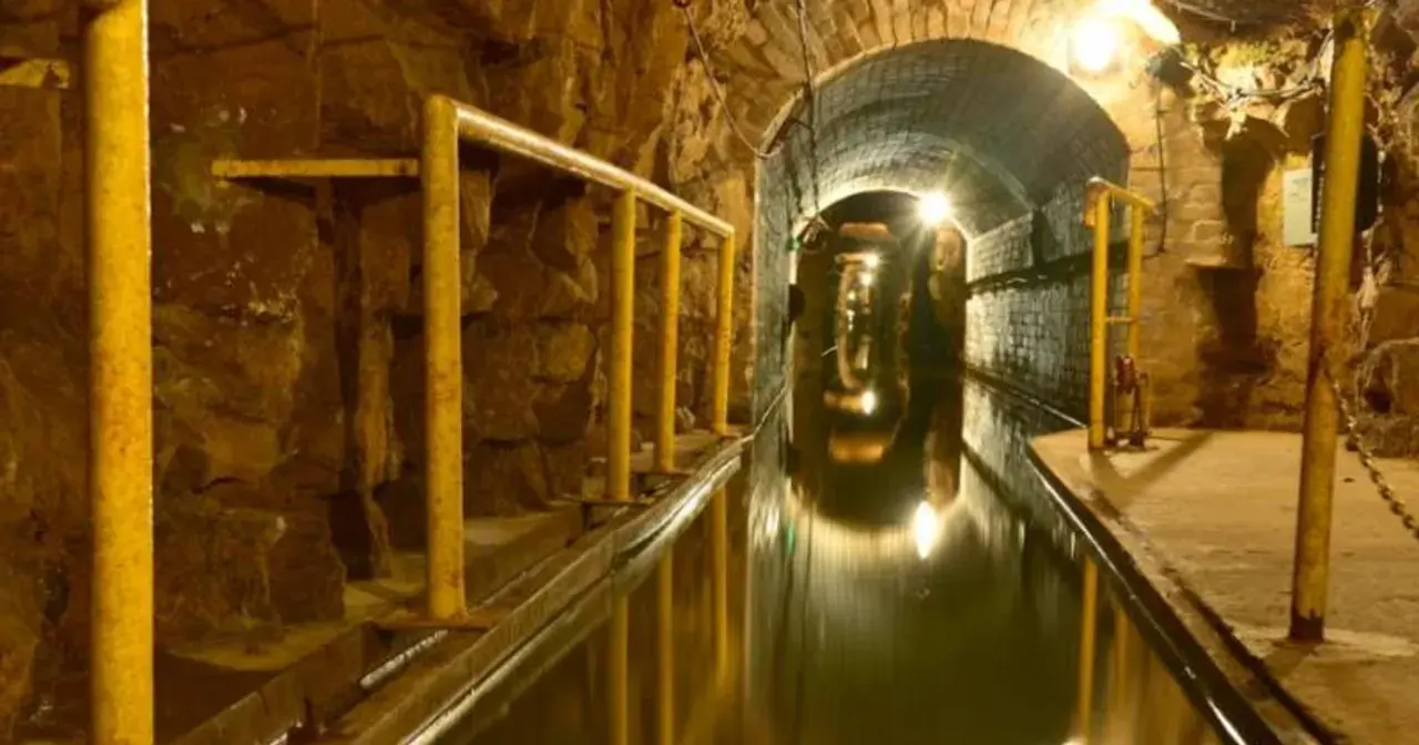 Podziemny tunel z wodą i żółtymi poręczami, idealny na zwiedzanie kopalni.