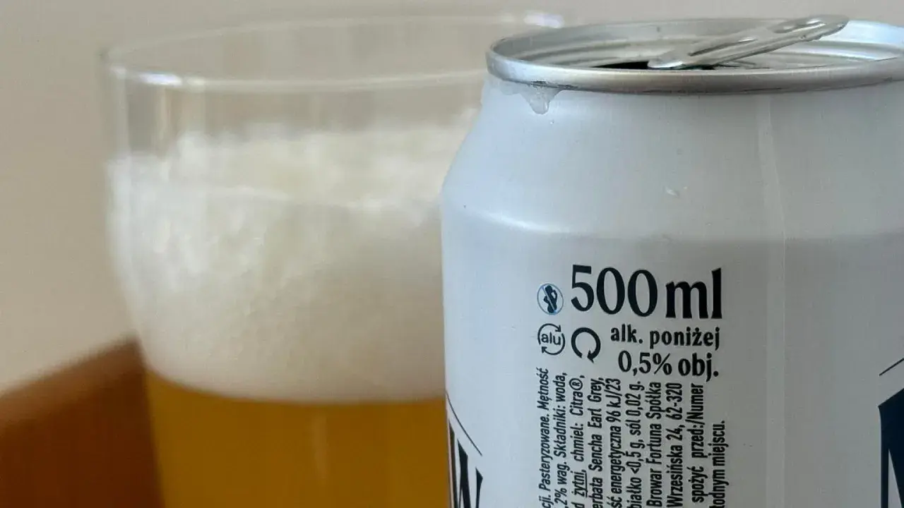 Piwo z puszki z etykietą "alk. poniżej 0,5% obj." obok szklanki z pianką. Sprawdzamy, ile promili ma to piwo.