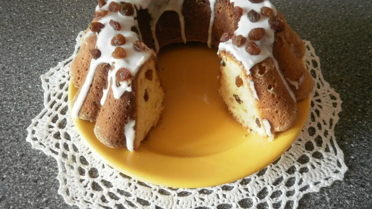 Pyszna babka drożdżowa z rodzynkami, polana lukrem i ozdobiona bakaliami, prezentuje się apetycznie na żółtym talerzu.
