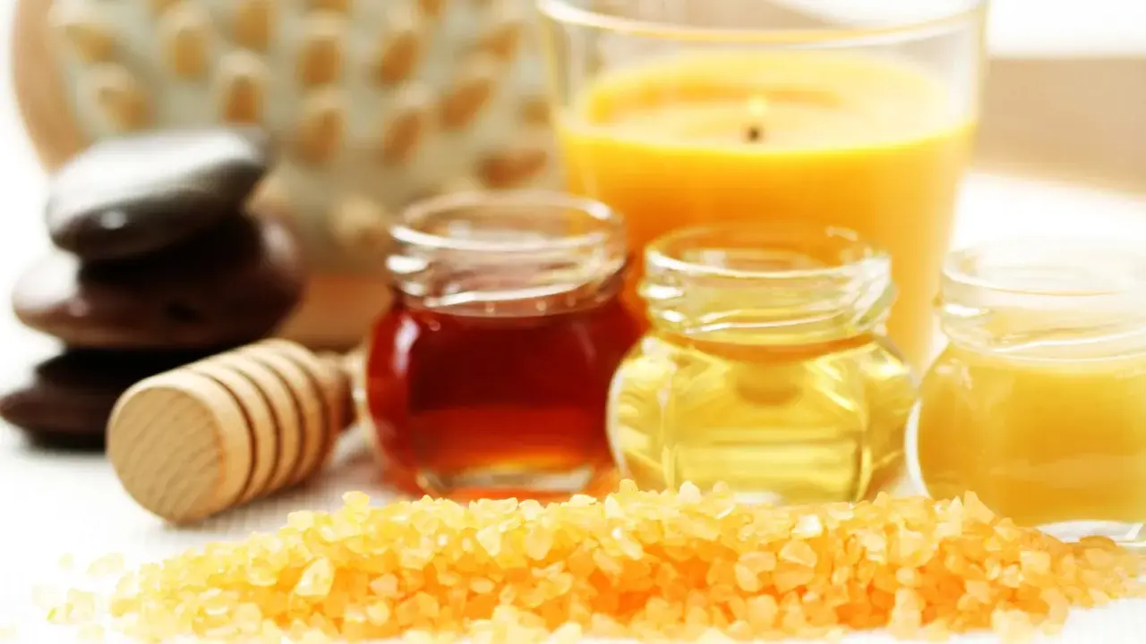 Ingredientes para un exfoliante corporal casero: sales, miel, aceites y una vela aromática.