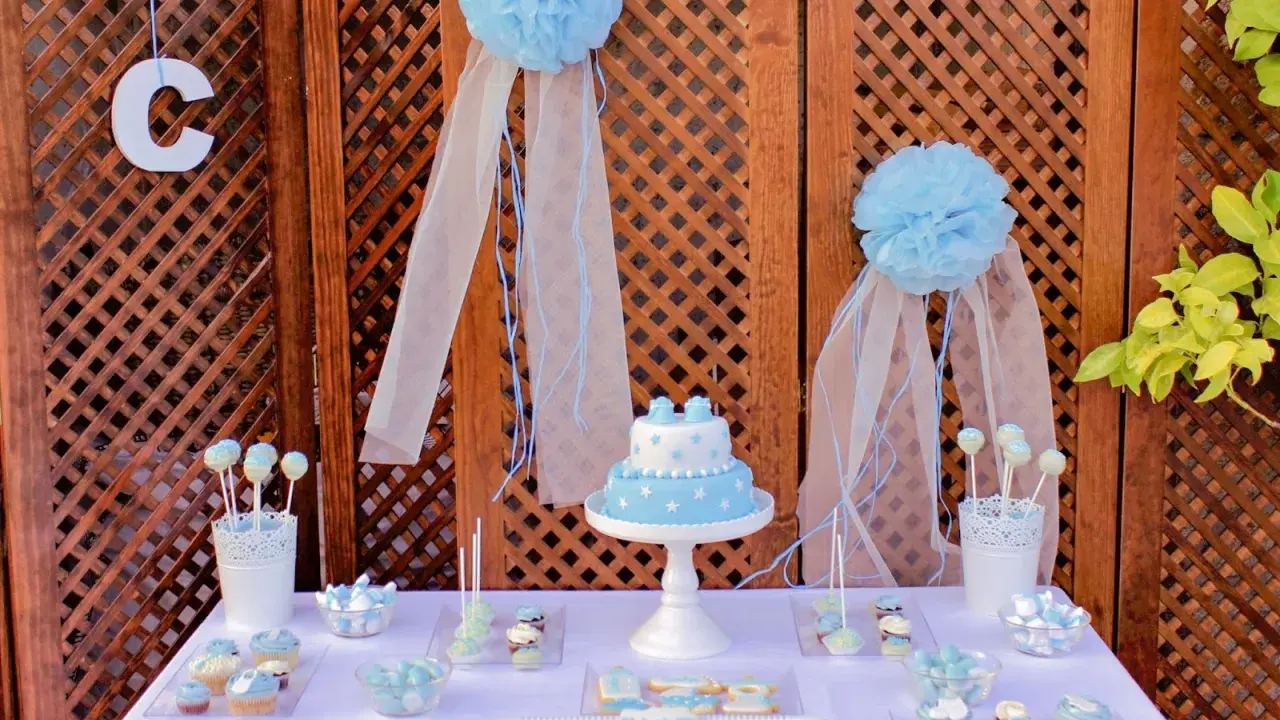 Mesa dulce bautizo casera con pastel, galletas y cupcakes decorados en tonos azules.