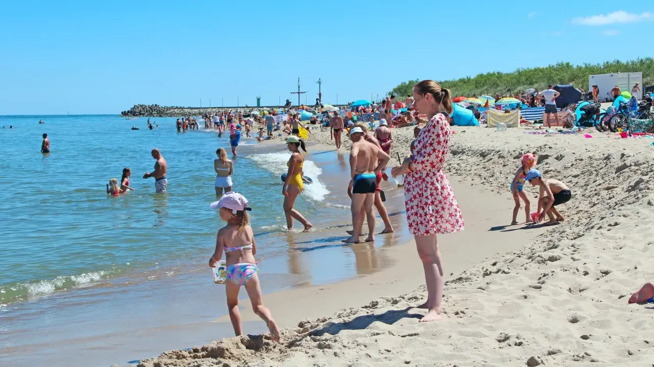 Słoneczne wczasy pod gruszą na plaży. Ludzie kąpią się w morzu i opalają na piasku. Dzieci bawią się w wodzie i budują zamki z piasku.