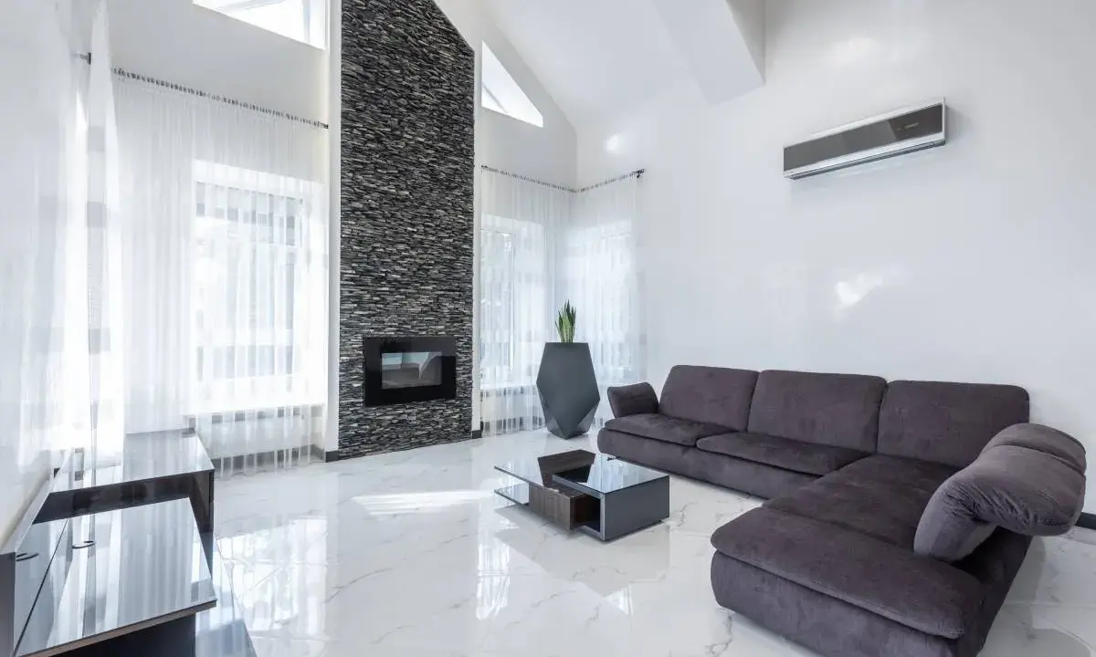 Sofá gris oscuro, chimenea de piedra, mesa de centro y suelo de mármol blanco.