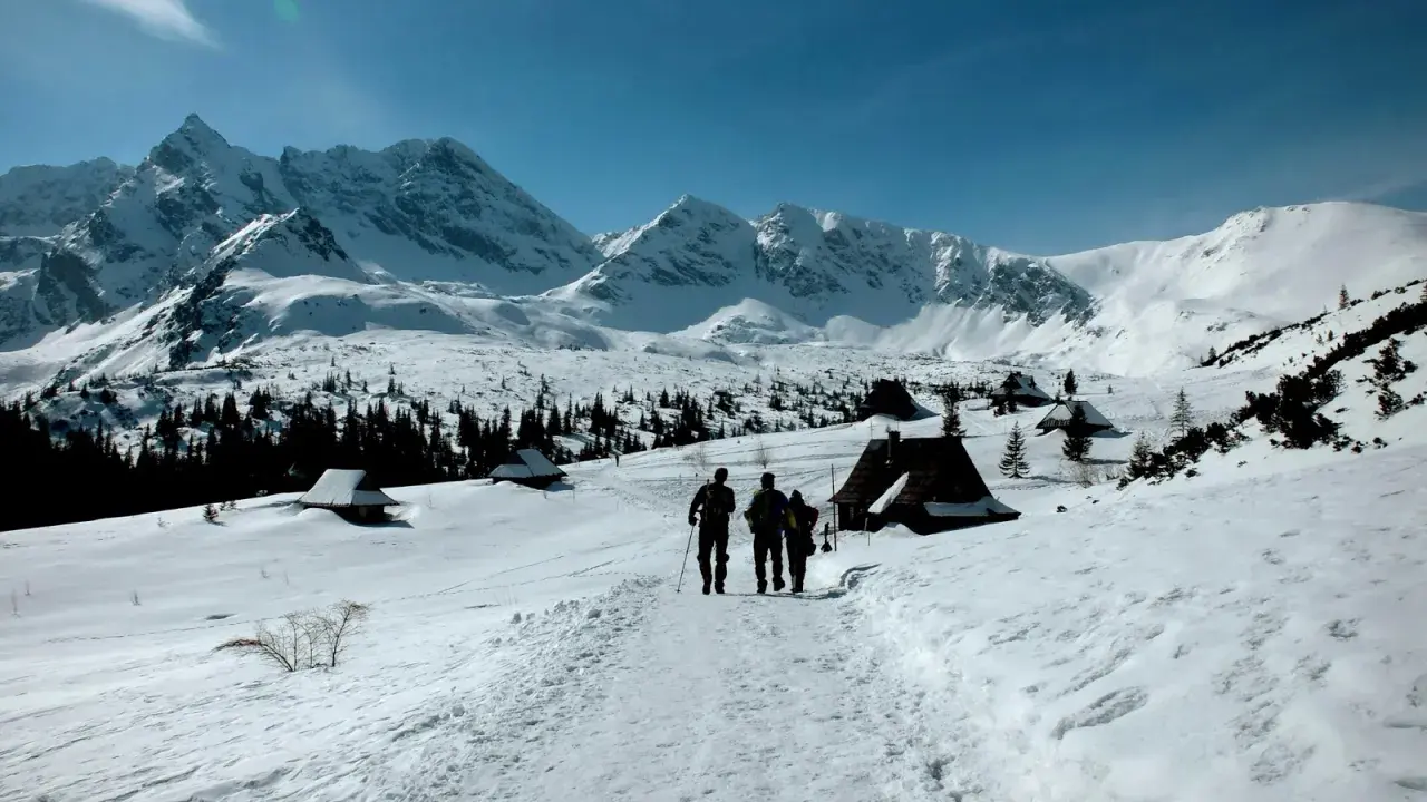 Trzej turyści idą szlakiem przez zasypane śniegiem Tatry. Widok idealny na tatry zimą dla średniozaawansowanych.