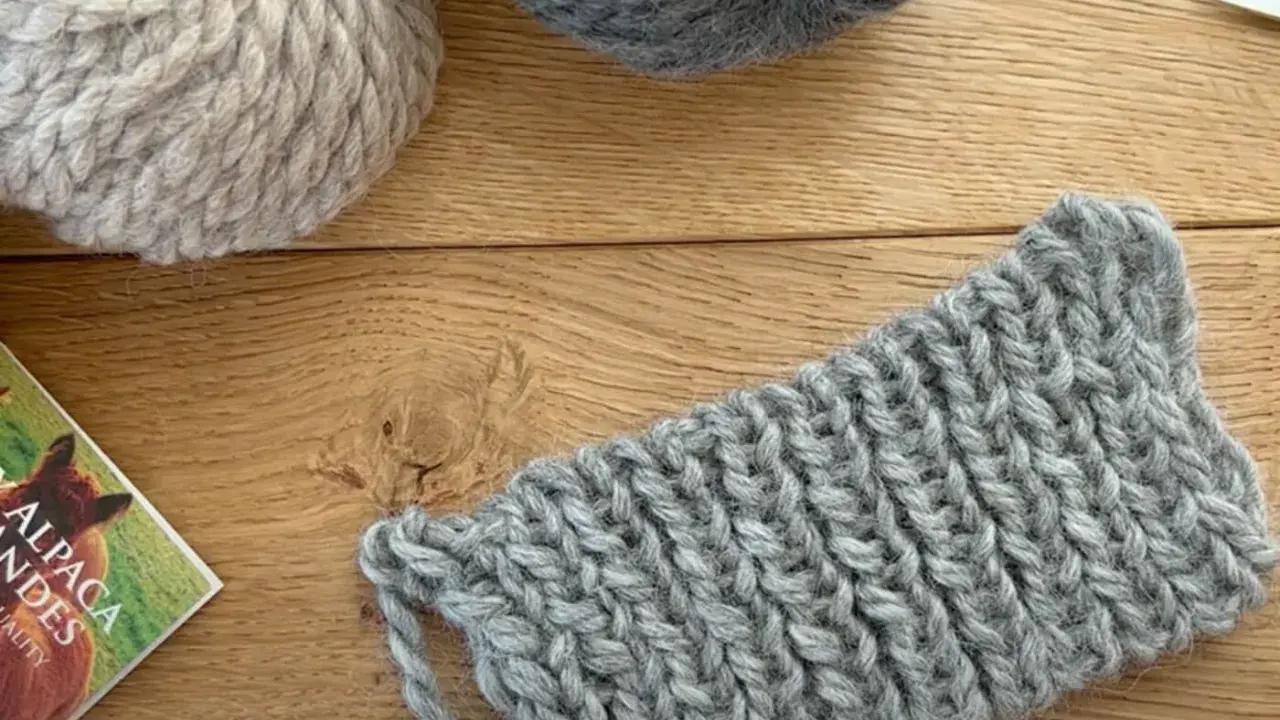 Ovillos de lana gris y beige sobre madera. Un trozo de tejido con puntos de lana muestra la textura.