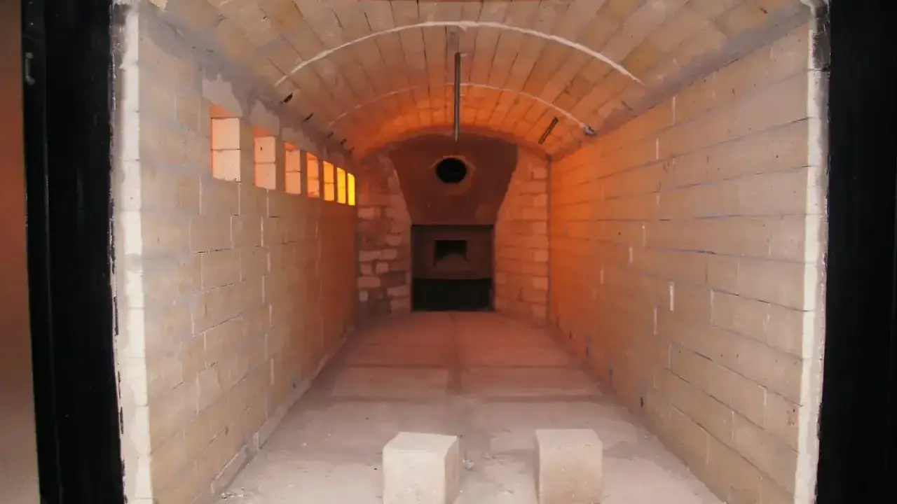 Wnętrze krematorium, gdzie czeka całun do kremacji. Pomieszczenie wyłożone cegłami, z łukowym sklepieniem i widocznym otworem pieca.