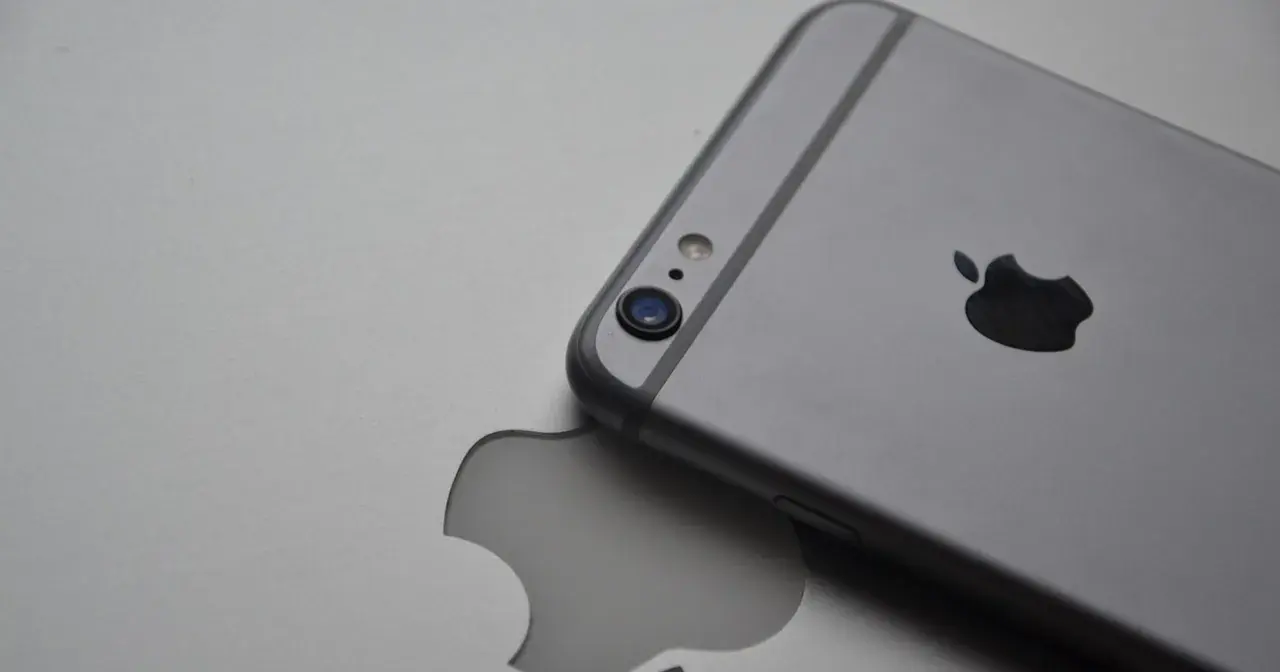 Srebrny iPhone leży na tle z wyciętym logo Apple, symbolizując spójność ekosystemu Apple.