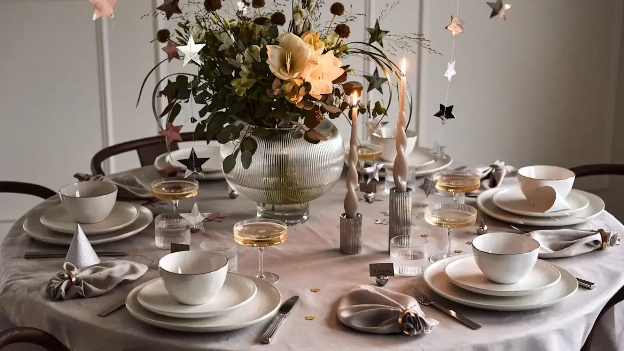 Vacker nyårsdukning med guldiga stjärnor, ljus och blommor. En elegant dukning för en festlig kväll.