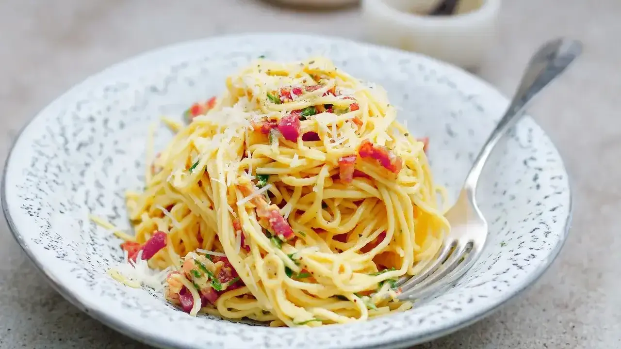 Pyszna carbonara ze śmietaną, okraszona boczkiem i parmezanem, czeka na widelcu.