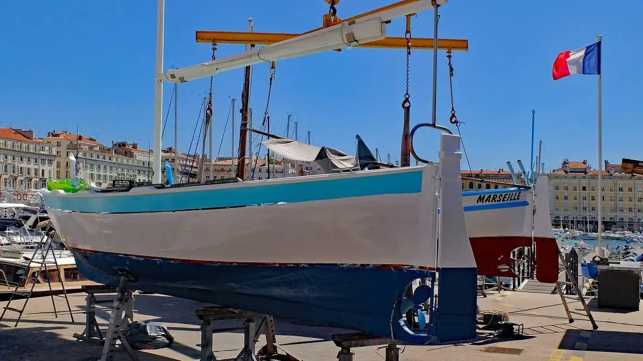 Un bateau hors de l'eau, prêt pour la maintenance, avec le nom "MARSEILLE" peint sur sa coque. Le drapeau français flotte au loin.