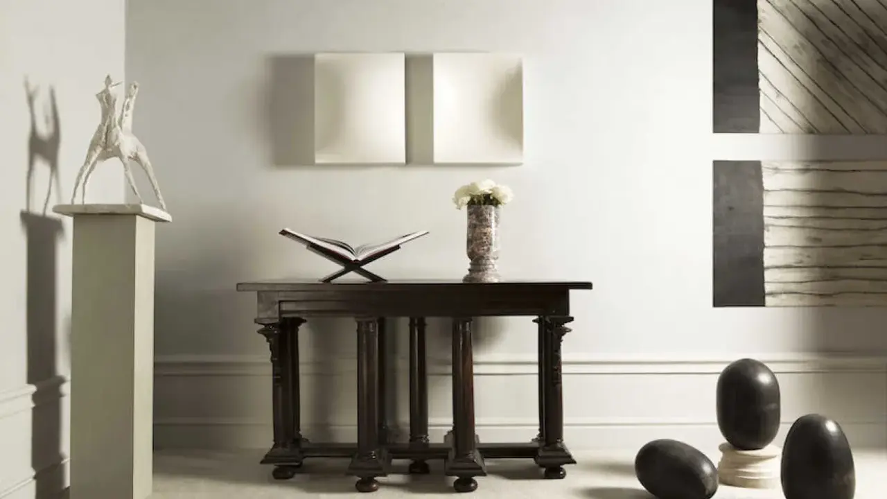 En elegant inredning med en skulptur av Claes Dahlen, en öppen bok, blommor i en vas och mörka stenägg.