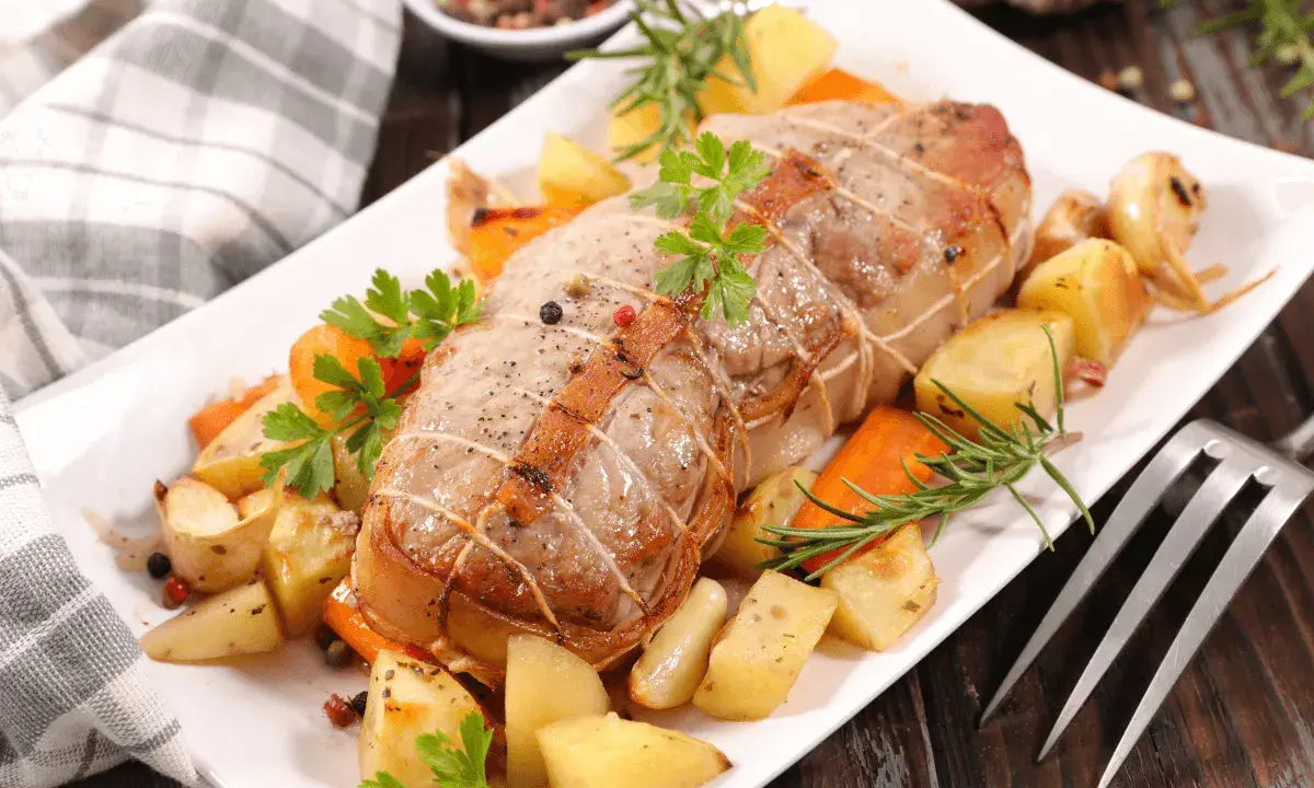 Rôti de veau savoureux, entouré de pommes de terre rôties, carottes et herbes aromatiques, prêt à être dégusté.