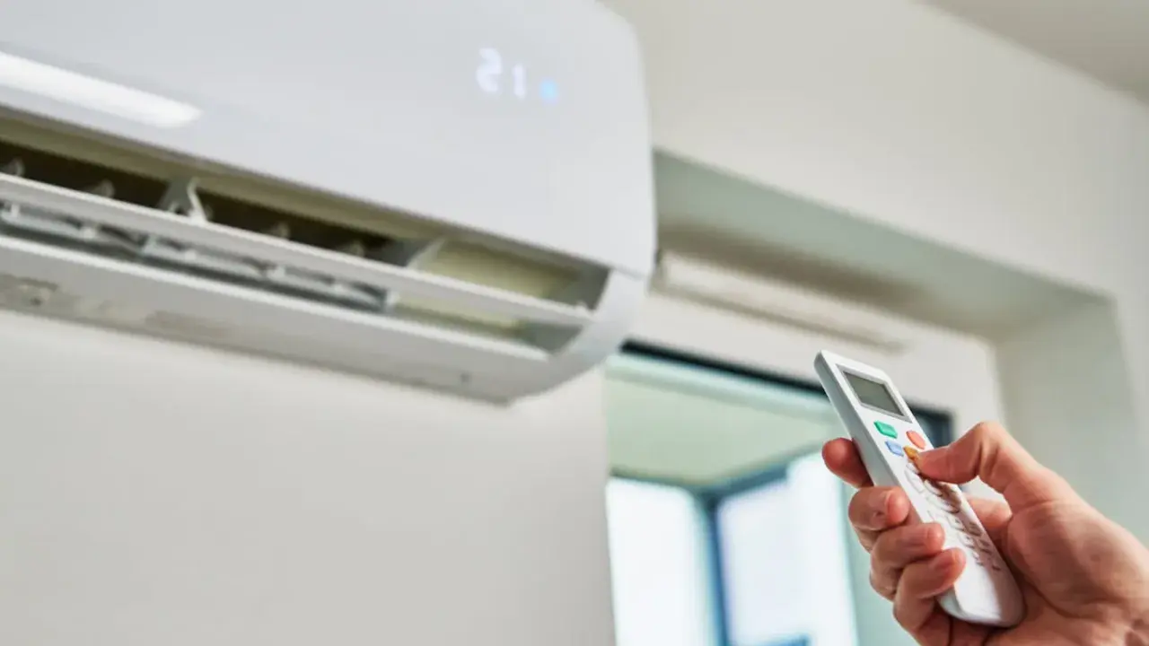 Mano con control remoto ajustando el aire acondicionado a 21 grados. ¿Es mejor apagar el aire acondicionado o dejarlo encendido?