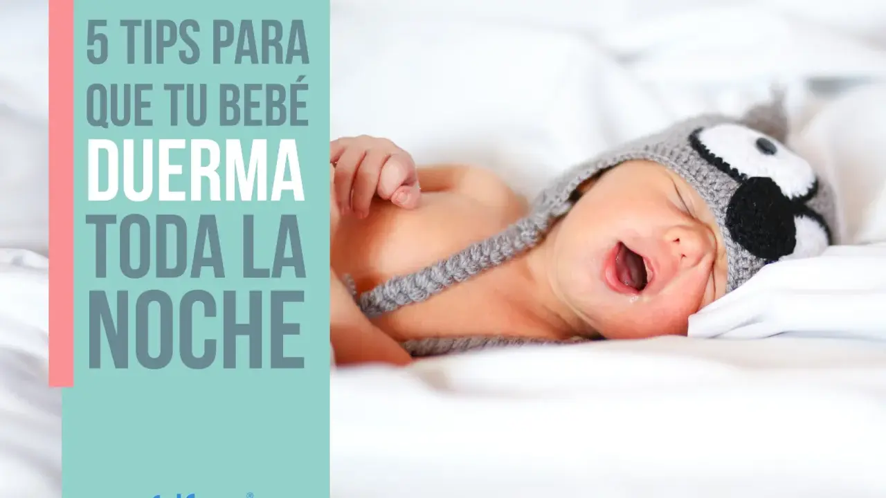 Un bebé con gorro de búho, con la boca abierta, en la cama. 5 consejos para que tu bebé duerma toda la noche.