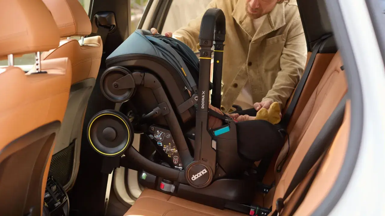 Mężczyzna wyjmuje fotelik z isofix z samochodu. Widać uchwyt i koła fotelika.