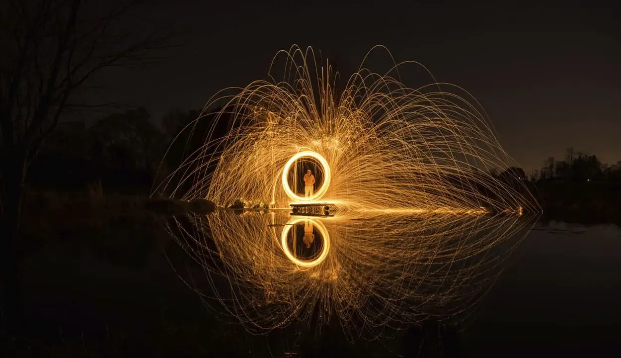 Un cerchio di scintille dorate, un uomo al centro, riflette sull'acqua. Un'opera d'arte che sembra **disegnare con la luce** nel buio della notte.