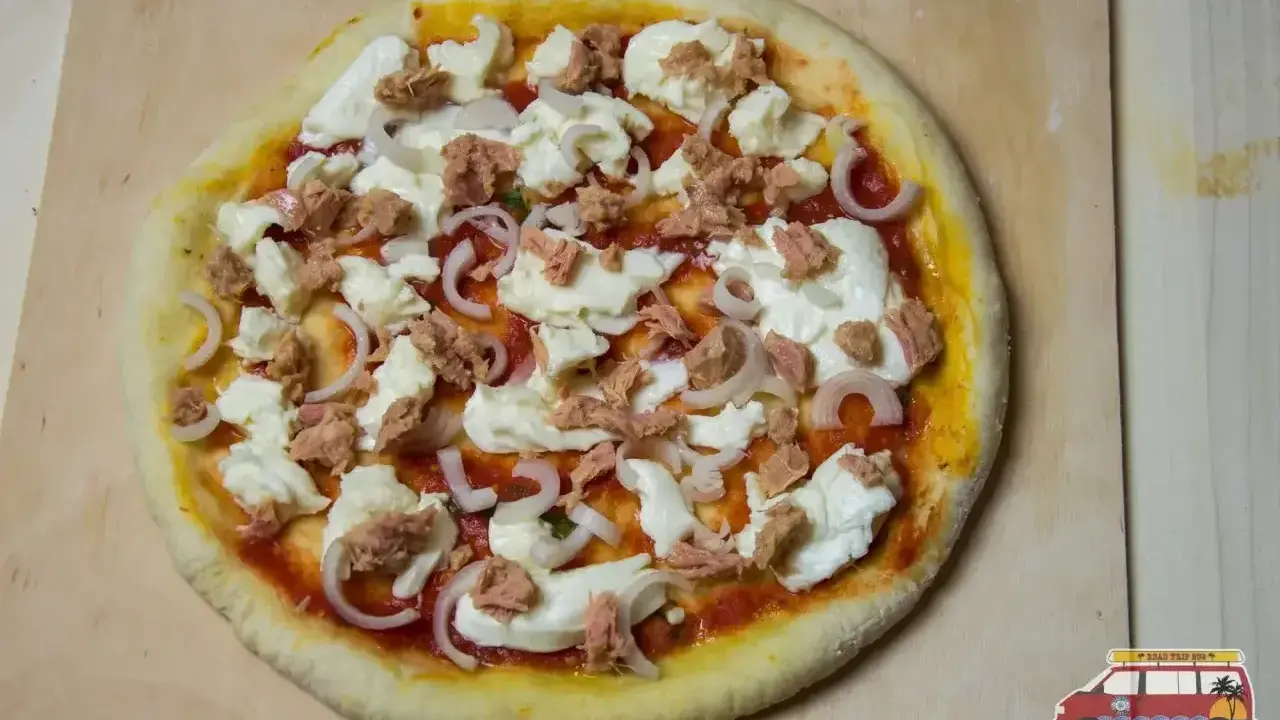 Gotowa do pieczenia pizza z tuńczykiem, mozzarellą i cebulą na drewnianej desce.
