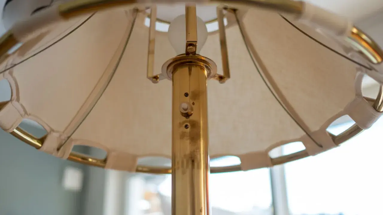 Detaljbild av en golvlampa i mässing från Ateljé Lyktan. Skärmen är av tyg med mässingsdetaljer.