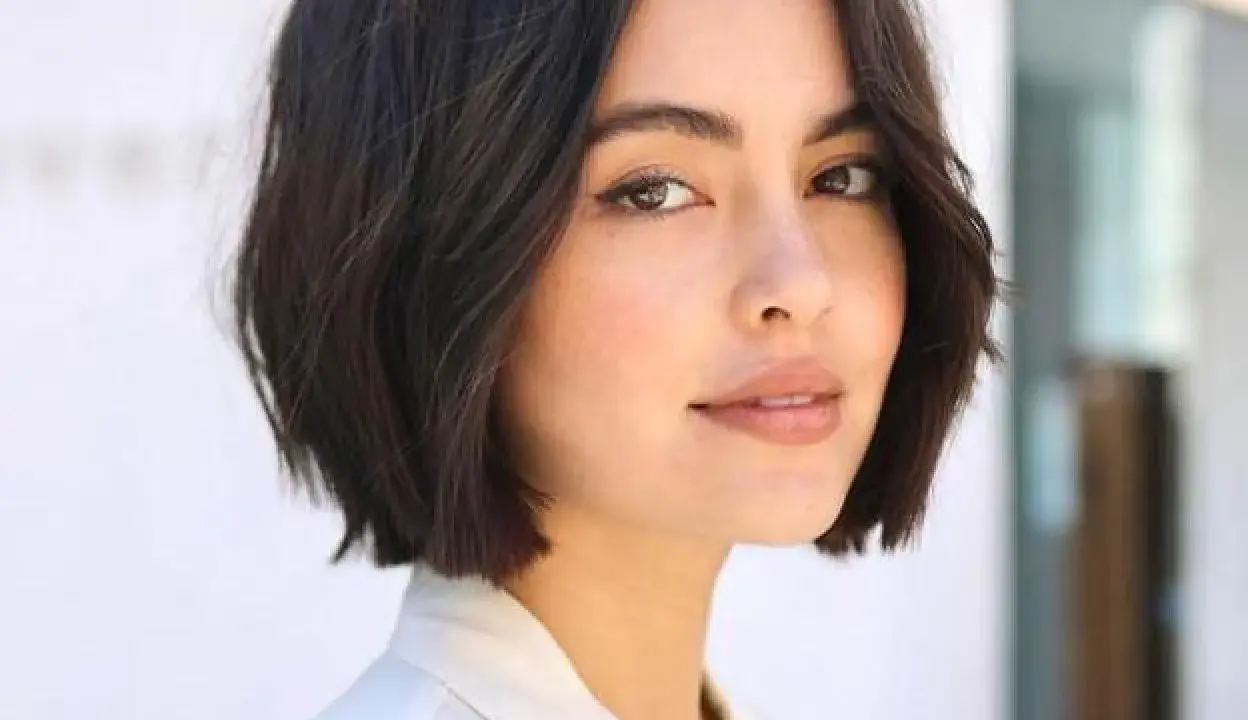 Mujer con un moderno corte de pelo bob oscuro y ondulado, luciendo un estilo chic y juvenil.