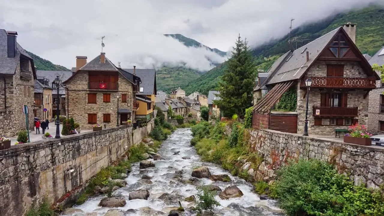 Ein rauschender Fluss schlängelt sich durch das malerische Val d'Aran, gesäumt von traditionellen Steinhäusern und grünen Bergen.