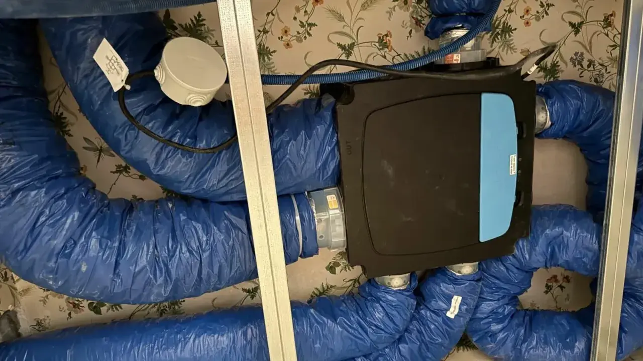 Système VMC installé dans un faux plafond. Les gaines bleues isolées sont connectées à une unité centrale noire. Un bon choix de VMC est essentiel pour la qualité de l'air intérieur.