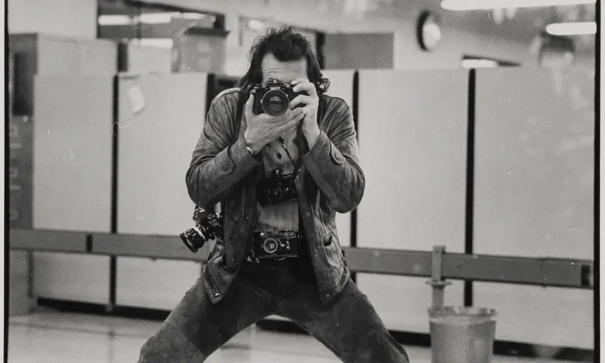 Un uomo con più macchine fotografiche al collo, intento a scattare un autoscatto. Un'immagine che cattura l'essenza di un fotografo, forse lo stesso René Burri.