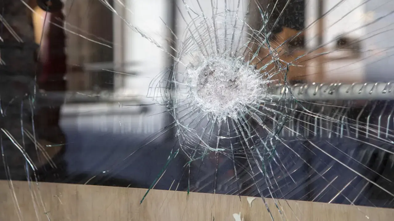 Une étoile de verre brisé se propage à travers la vitre, révélant un monde flou derrière.
