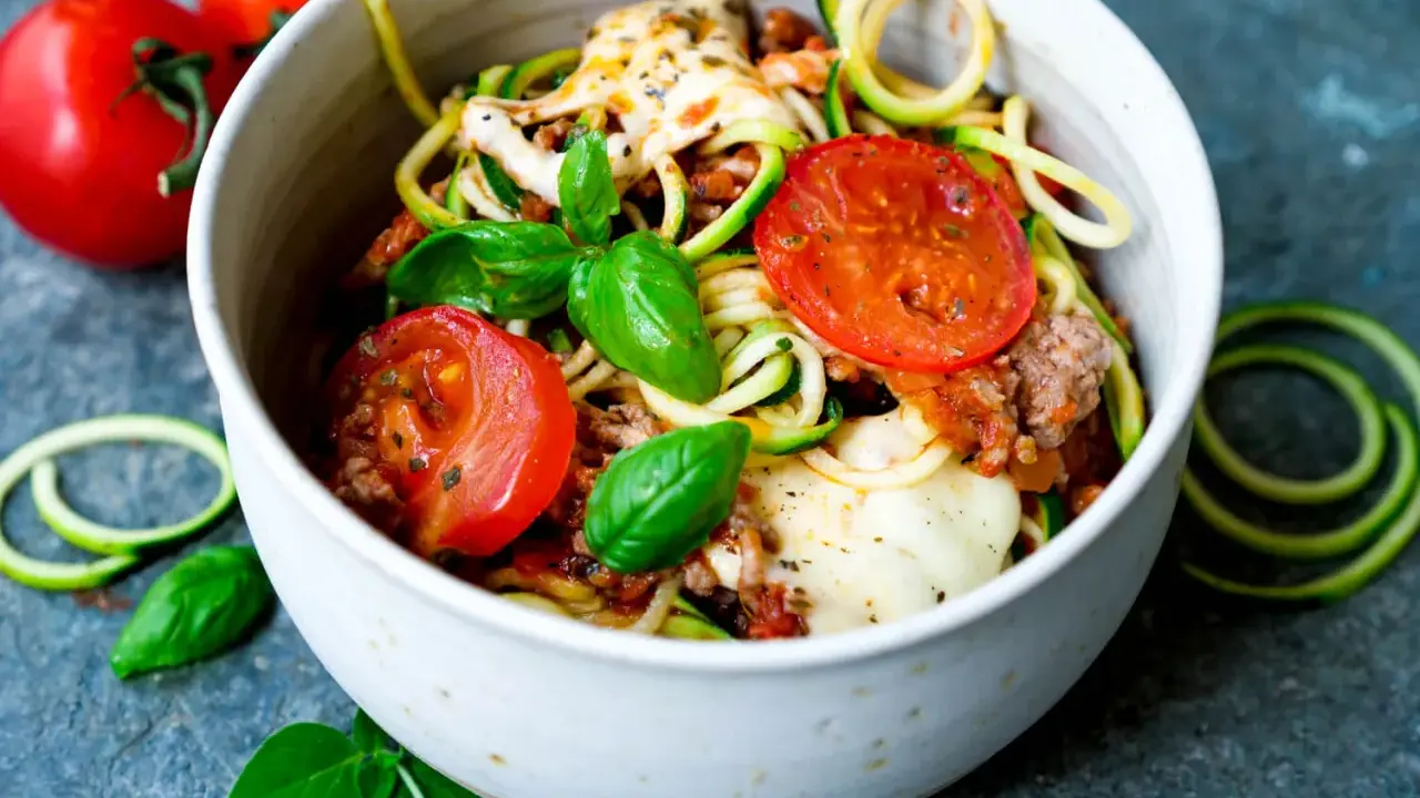 Herzhafte rezepte mit zucchini und hackfleisch: Zoodles mit Hackfleischsauce, Tomaten und geschmolzenem Käse, garniert mit frischem Basilikum.