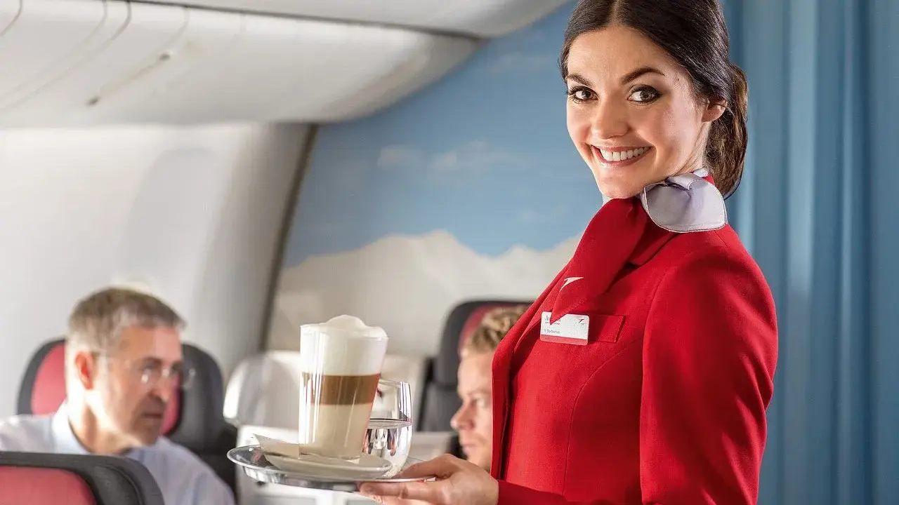 Uśmiechnięta stewardessa w czerwonym mundurku podaje kawę. Czy jej stewardessa zarobki są wysokie?