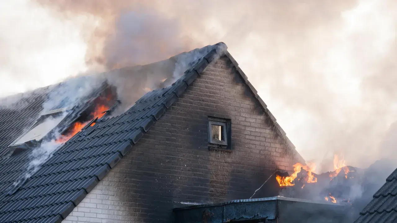 Un incendie maison ravage le toit, des flammes vives et une épaisse fumée s'échappent des tuiles.