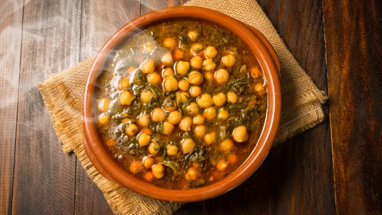 Cazuela de barro con garbanzos y espinacas, humeante y lista para servir. Se puede poner cazuela de barro en la vitro para cocinar este delicioso plato.