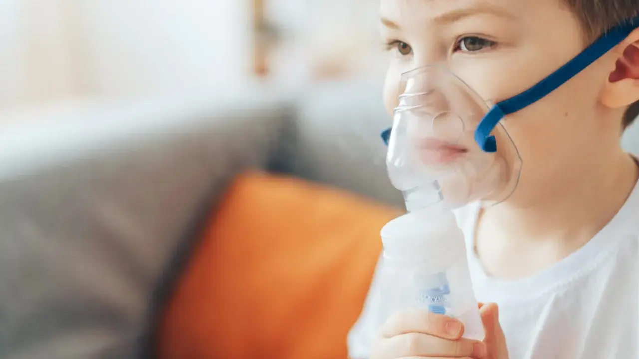 Chłopiec z maską inhalacyjną na twarzy, korzystający z nebulizatora. Pomaga mu to w leczeniu kataru.