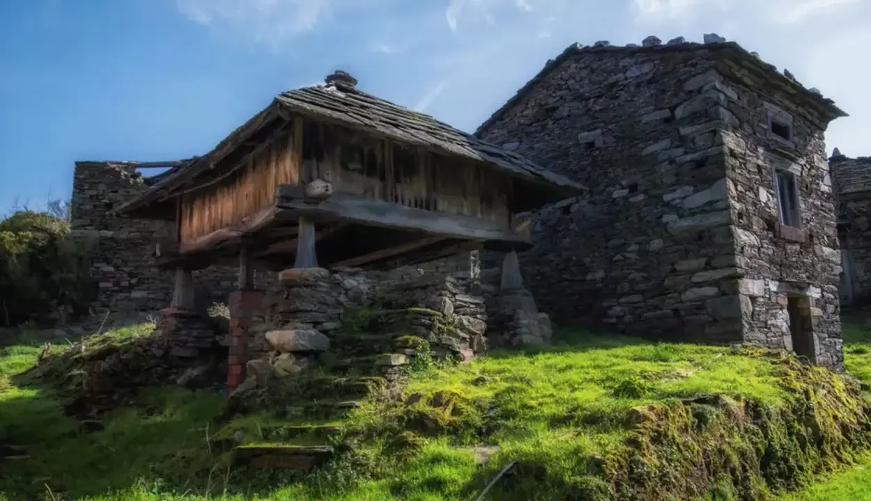 Antiguos hórreos de piedra y madera, testigos de la ruta del silencio. Hierba verde y cielo azul.