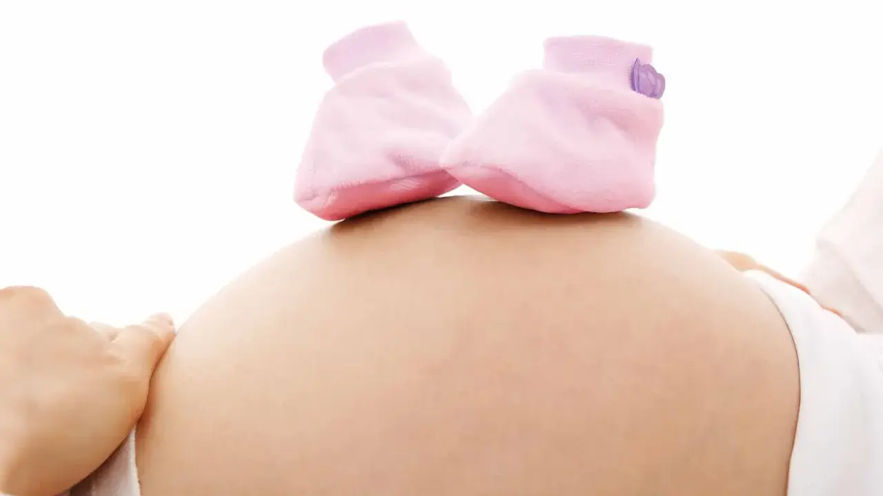 Close-up of a pregnant belly with tiny pink baby booties on top.