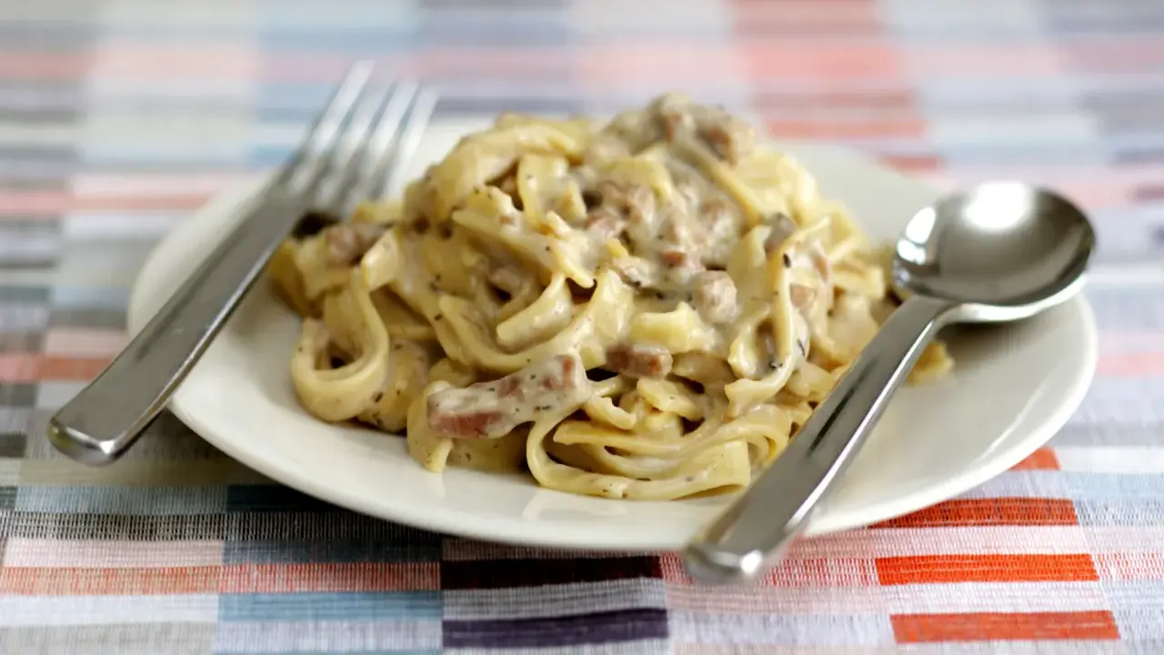 Un piatto di tagliatelle ai funghi cremose, pronte per essere gustate con forchetta e cucchiaio.
