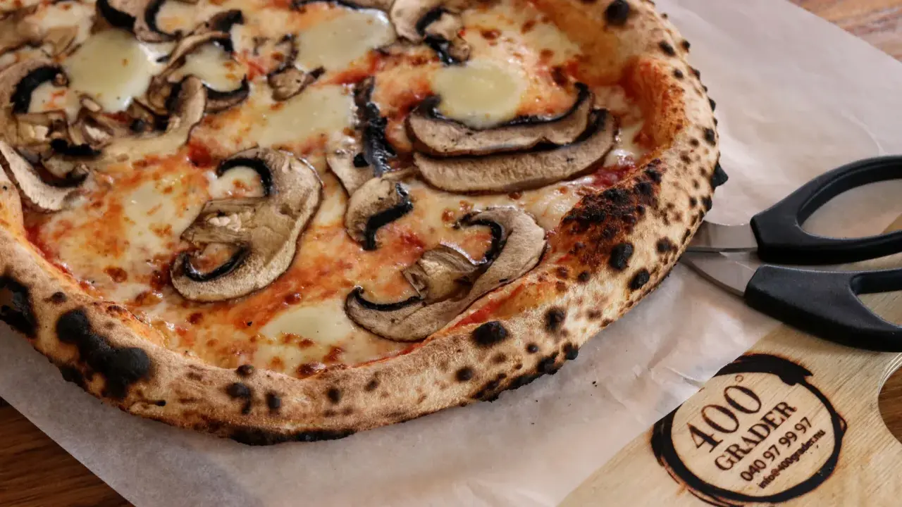 En nybakad champinjonpizza med bubblande ost, redo att skäras med saxen. En perfekt pizza för alla som gillar 400grader recensioner.
