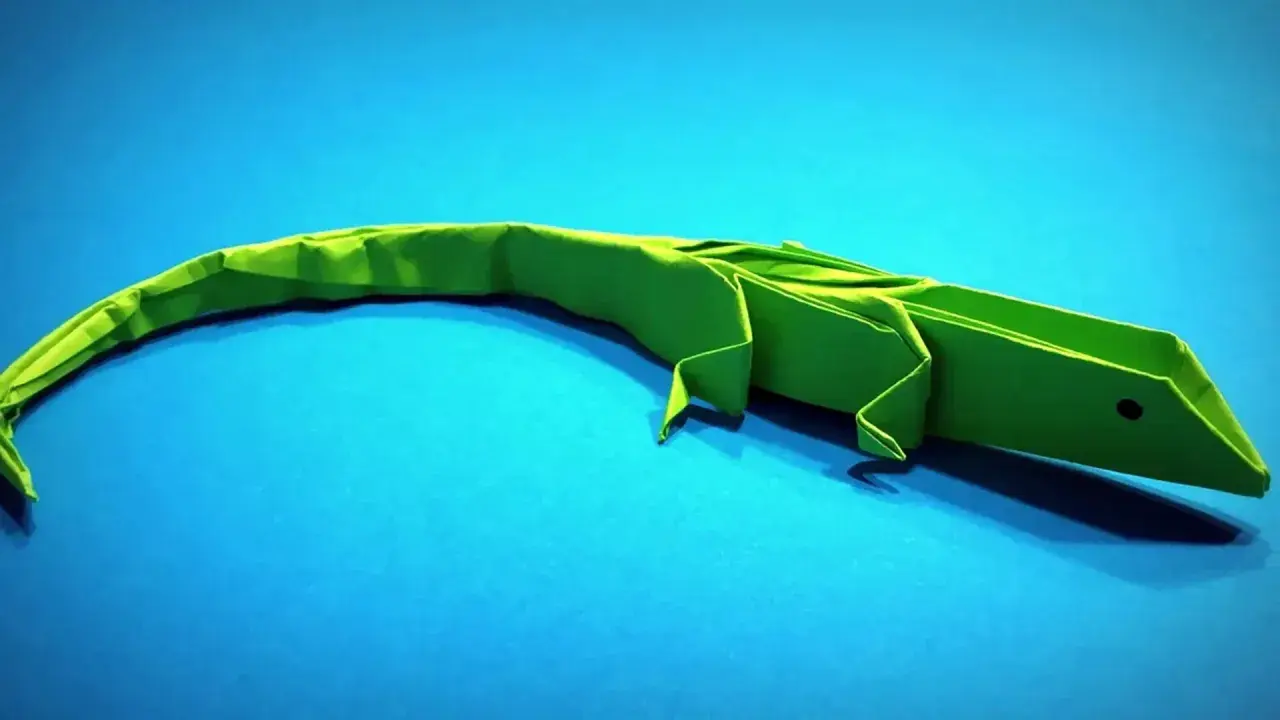 Un lagarto verde de papiroflexia animales descansa sobre un fondo azul.