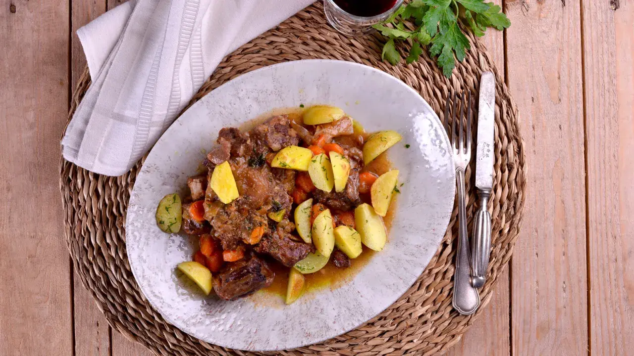 Plato de rabo de toro estofado con patatas y zanahorias, bañado en una salsa de vino blanco.