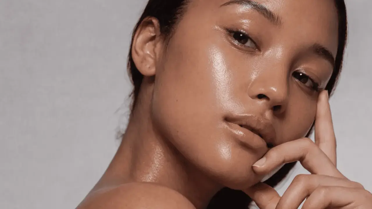 Rostro de mujer con piel glowy, hidratada y radiante. Su mano acaricia suavemente su barbilla.