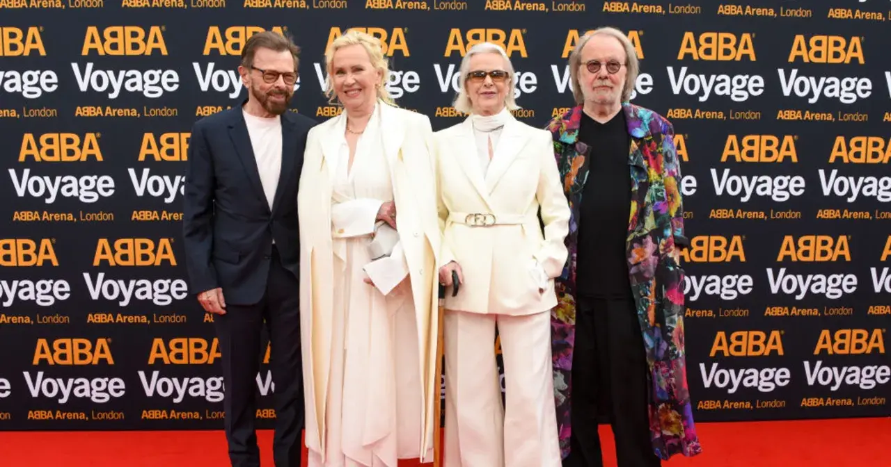 Członkowie zespołu ABBA na czerwonym dywanie, pozujący do zdjęć przed banerem "ABBA Voyage".