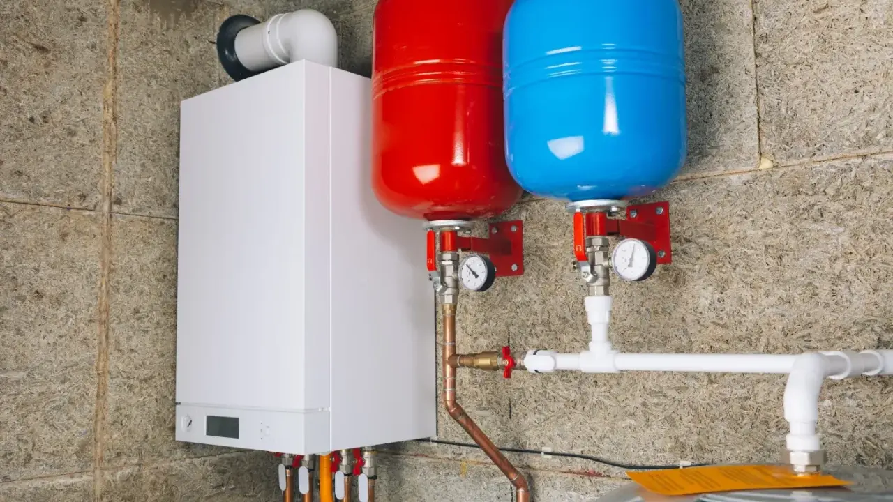 Nowoczesny kocioł z dwoma zbiornikami (czerwonym i niebieskim) i instalacją hydrauliczną. To przyszłość ogrzewania, bo zakaz pieców gazowych zbliża się wielkimi krokami.