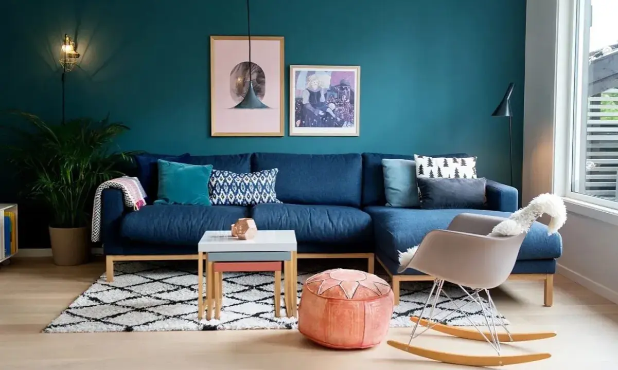 Un accogliente salotto con divano blu, tappeto a rombi e pareti color ral ottanio.