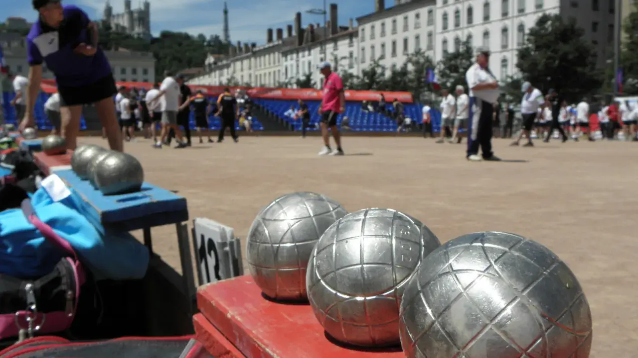 Boules de jeu en gros plan, prêtes pour une partie de boule lyonnaise. Des joueurs s'affrontent en arrière-plan.