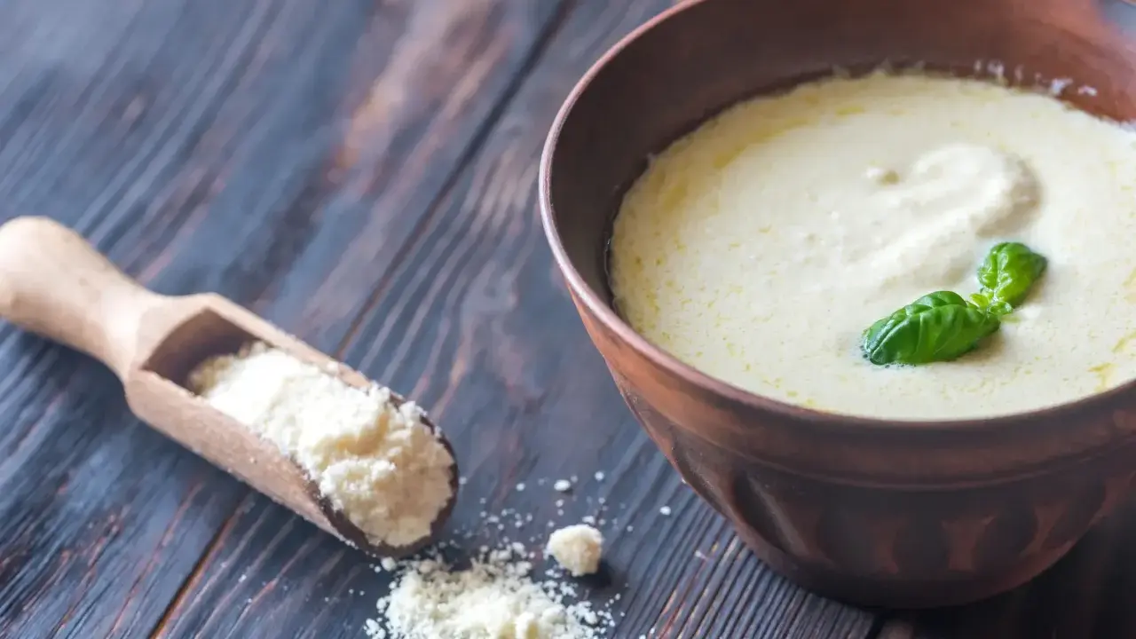 Sauce crémeuse à la sauce parmesan italienne, garnie de basilic frais. Une cuillère en bois contient du parmesan râpé.