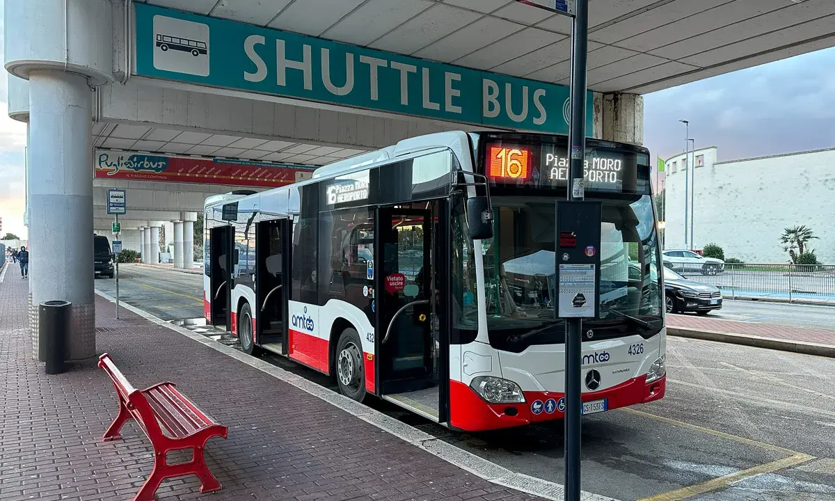 Autobus wahadłowy na przystanku lotnisko. Czerwona ławka czeka na pasażerów.