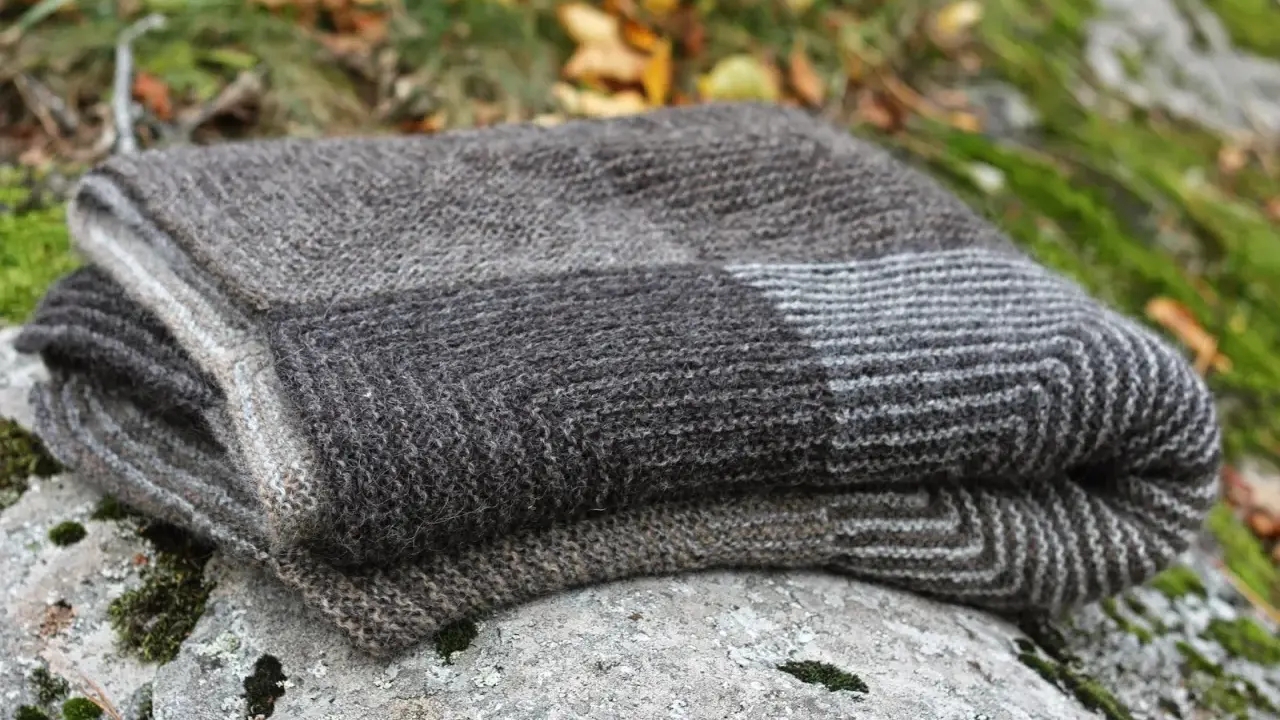 En hopvikt, handstickad filt i gråa nyanser ligger på en mossig sten. Perfekt för mysiga höstkvällar.